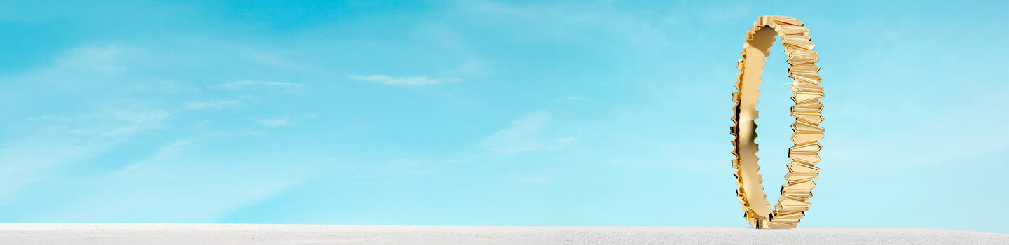 Birks Beekeeper yellow gold bangle on a blue background.